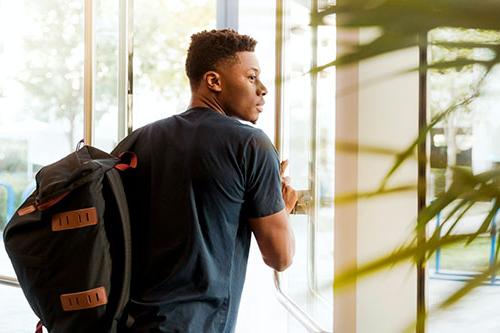 年轻的非裔美国男学生背着背包走进门来